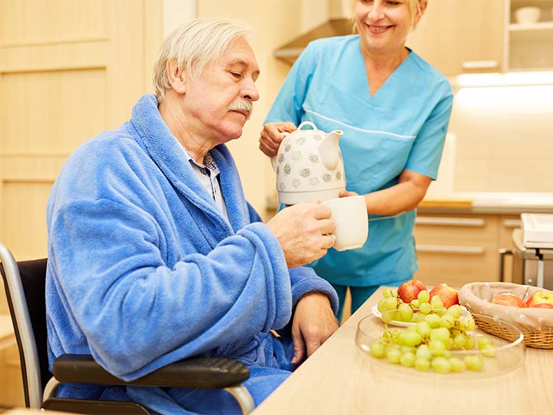 Pflegepersonal vom Pflegedienst in Düren versorgt einen älteren Herren mit Essen und Getränken