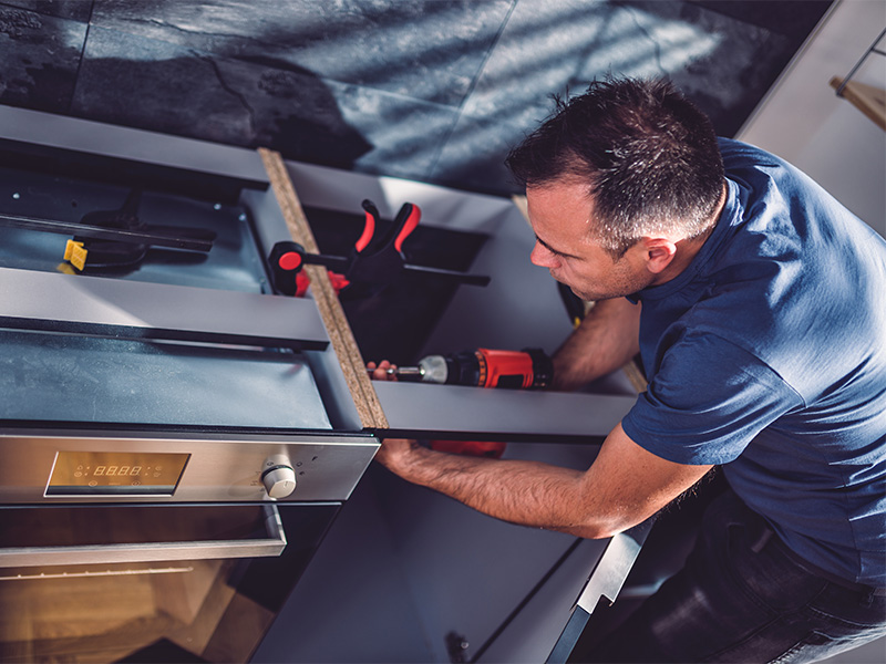 Fachmann montiert Küchenschränke mit Akku-Bohrmaschine bei einer professionellen Küchenmontage in Wohnraum.