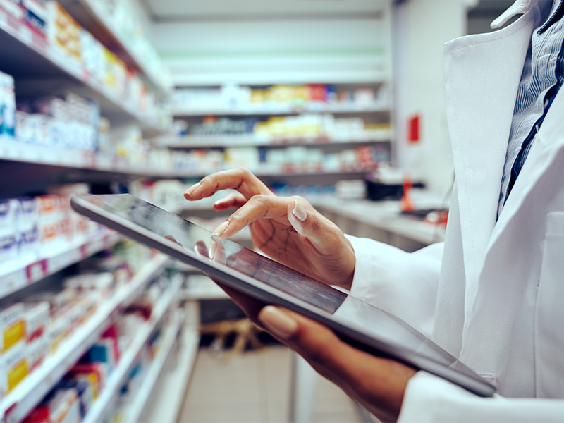 Apothekerin pr&uuml;ft Medikamentenbestand mit digitalem Tablet in moderner Apotheke f&uuml;r effiziente Arzneimittelverwaltung